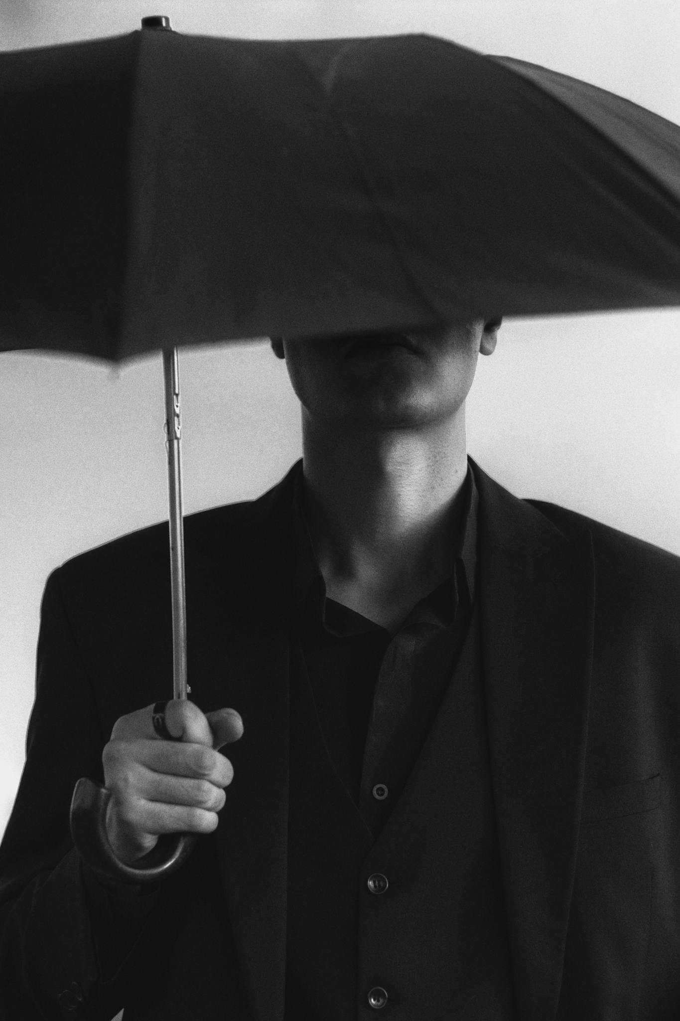 Elegant black and white image of a man in a suit holding an umbrella, evoking mystery and sophistication.
